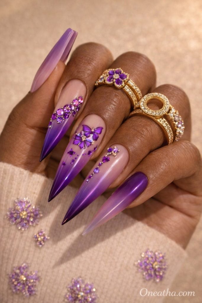 Purple butterfly nails with ombre fade, nude base acrylic nails, rhinestone accents, glossy stiletto nails, butterfly nail art design on warm-toned hand with gold rings, luxury nail inspiration
