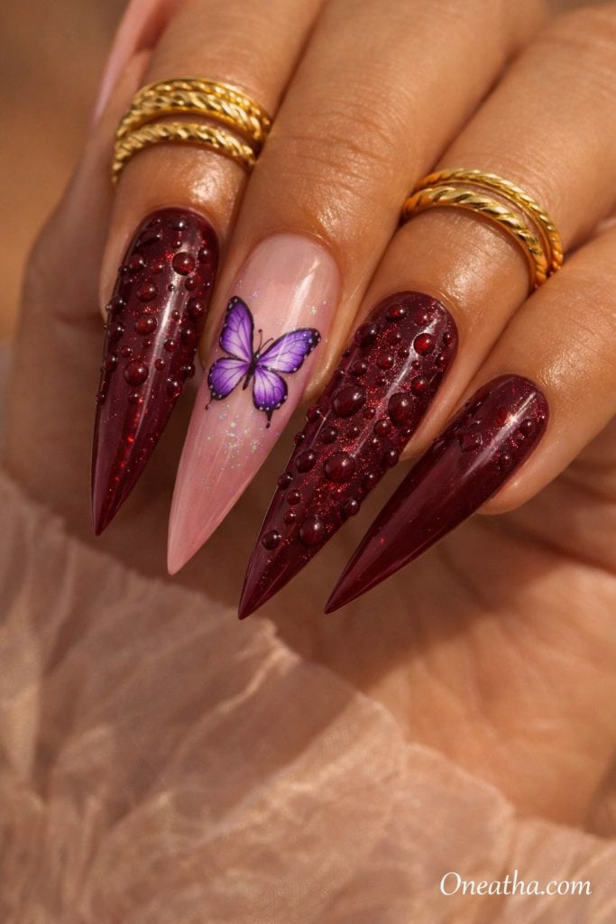 Purple butterfly nails with deep burgundy chrome nails, 3D water droplet nail art, nude accent nail with butterfly design, glossy stiletto acrylic nails, luxury dark burgundy and purple nail inspiration on warm-toned hand