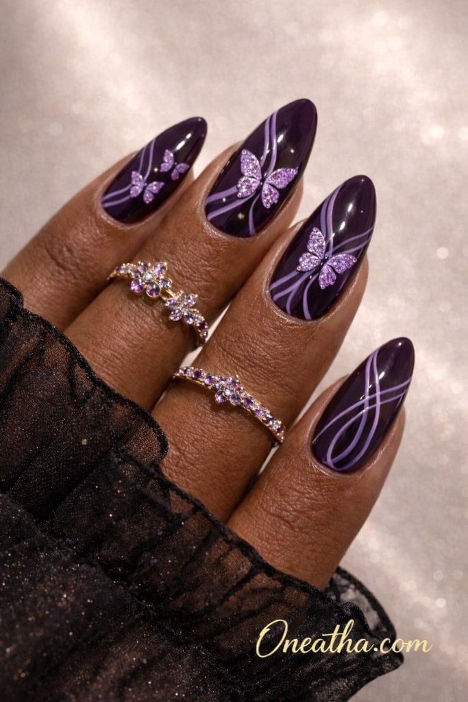 Purple butterfly nails with dark plum glossy base, lilac swirl line nail art, glitter butterfly accents, almond shaped acrylic nails, luxury nail design on warm-toned hand with gold rings