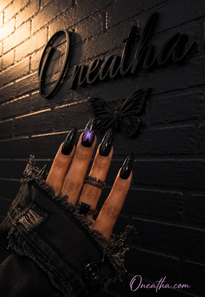 Black sparkly nails with purple butterfly accent.