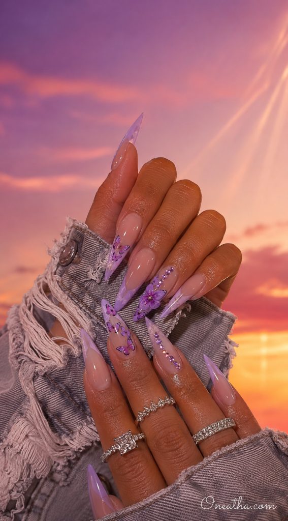 Lilac butterfly stiletto nails with hibiscus flowers and rhinestone accents.
