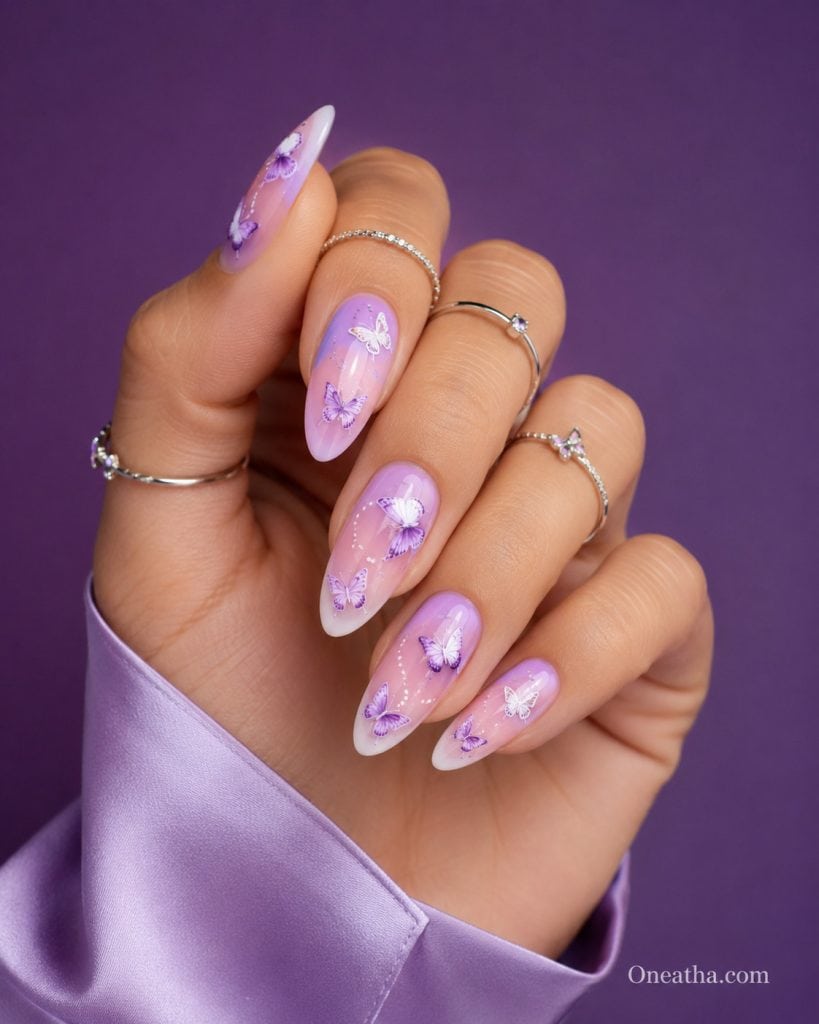 Oneatha luxury butterfly aura nails featuring almond-shaped lavender ombré nails, blush pink gradient, milky white French tips, hand-painted purple and white butterfly nail art, glossy editorial manicure, silver rings, lavender silk blouse, high-fashion beauty photography, feminine nail inspiration.