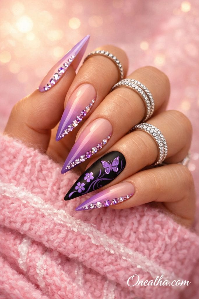 Butterfly Gemstone luxury stiletto nails by Oneatha featuring a purple pink aura ombre glow, nude sheer base, sparkling pink and purple gemstones, matte black accent nail with purple butterfly nail art, floral swirl designs, silver rings, pink sweater cuff, and soft sunlit luxury background.