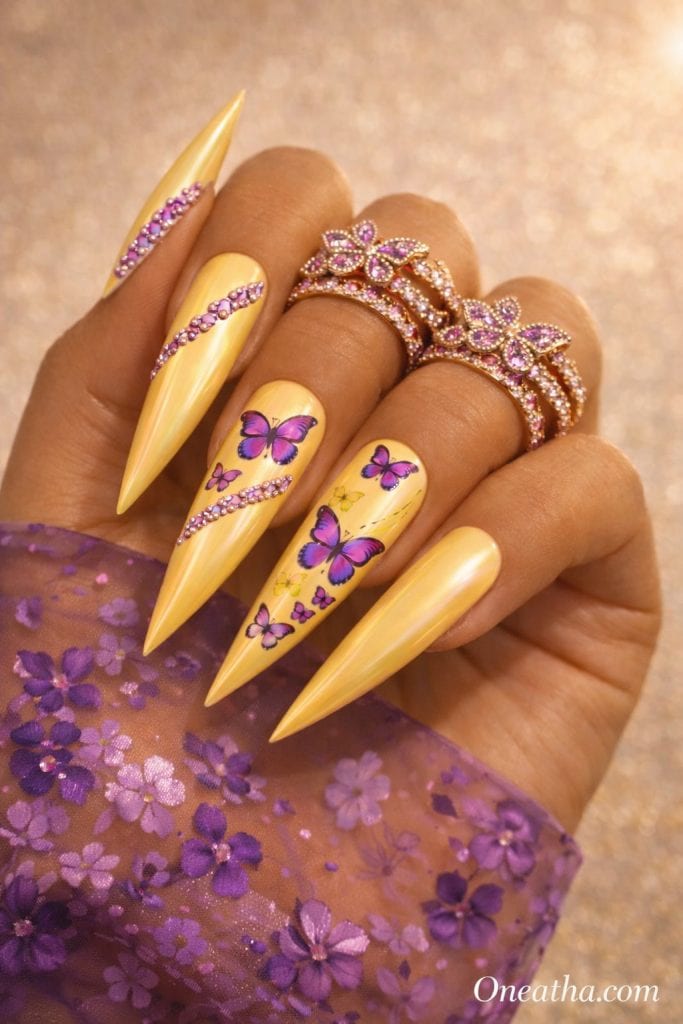Purple Monarch by Oneatha featuring yellow chrome stiletto nails with purple butterfly nail art, purple gemstones, luxury butterfly nails, and bold summer nail inspiration.