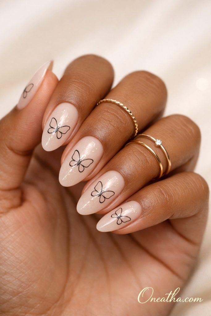 Nude butterfly nails with delicate black outline butterfly designs on glossy almond-shaped nails. Soft, minimal butterfly nail design with a clean, elegant finish and subtle shimmer.