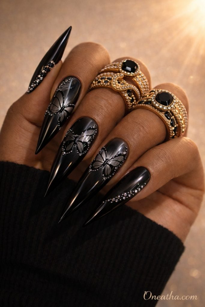 Black butterfly nails with chrome mirror finish and silver rhinestone accents on almond-shaped nails. Glossy black butterfly nail design with a luxury aesthetic and reflective high-shine detail.