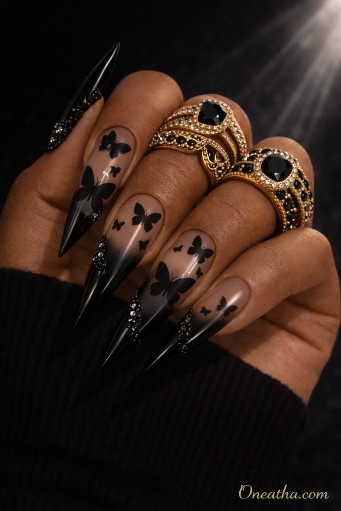 Black butterfly nails with matte butterfly designs over a sheer nude base and glossy black tips, finished with crystal accents. Elegant black butterfly nail art with a luxury aesthetic and high-contrast, polished finish.