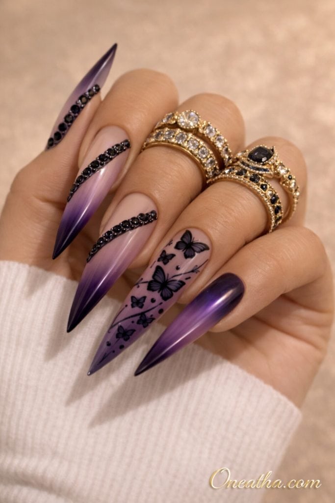 Purple ombré stiletto nails with black butterfly designs and rhinestone accents on a hand with gold rings and a neutral background. Elegant butterfly nail design with glossy finish and soft gradient for a modern, luxe manicure look.