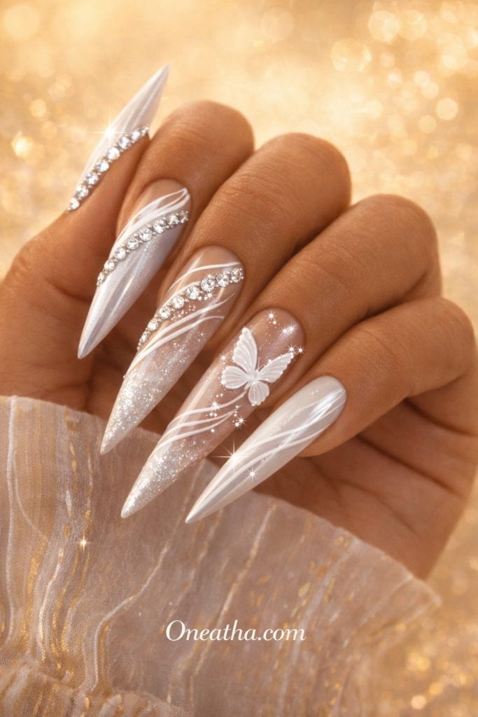 Close-up of a warm cinnamon-toned hand with long white stiletto nails featuring butterfly designs and sparkling gemstone accents. The nails have a glossy, glittery finish against a golden glowing background, creating a dreamy luxury aesthetic.
