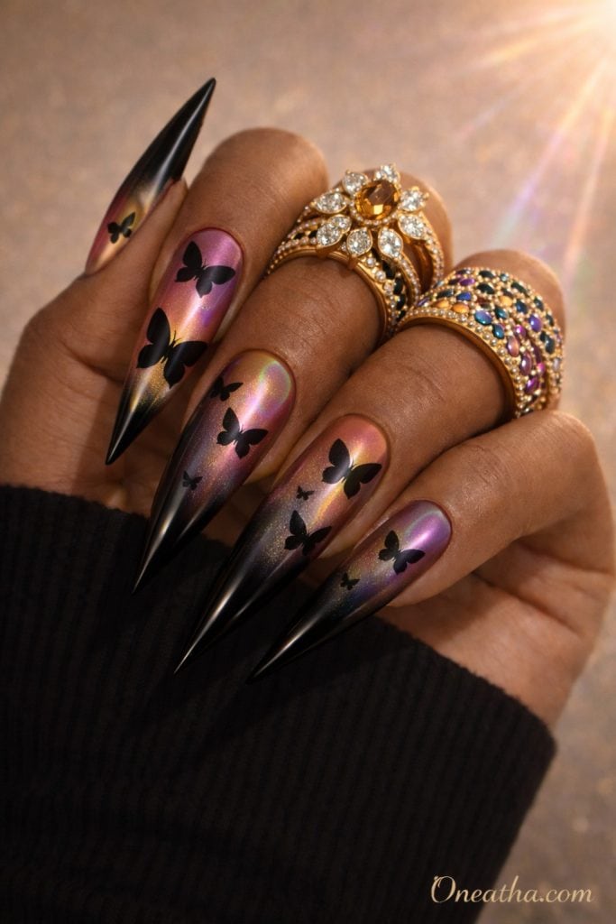 Black butterfly nails with rainbow chrome aura base shifting pink, purple, and gold tones on almond-shaped nails. Glossy black butterfly nail design with a luxury multichrome finish and luminous reflective detail.