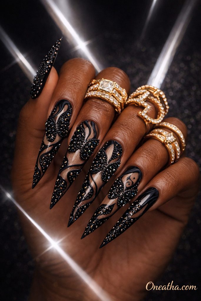 Black butterfly nails with black rhinestones forming butterfly shapes and abstract line detailing on long stiletto nails. Luxury black butterfly nail design with high shine, dimensional sparkle, and bold statement finish.