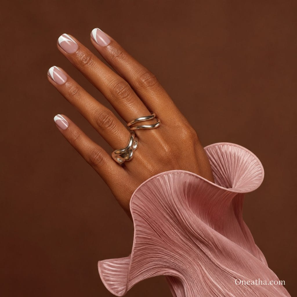 Luxury Luxe French nail design on short, neatly shaped nails featuring a modern white French tip. Set on a warm cinnamon-toned hand model with silver luxe rings and a soft pink blouse against a rich brown luxury background. The design is clean, minimal, and elegant, emphasizing a timeless beauty aesthetic and the versatility and charm of short nails.