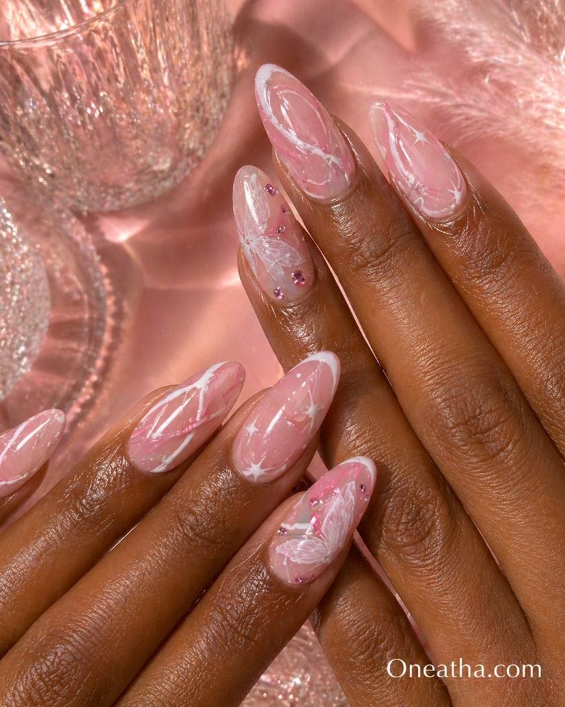 Butterfly nail designs by Oneatha featuring pink and white swirl lines, sparkling pink gemstones, and delicate butterfly accents on elegant pink nails.