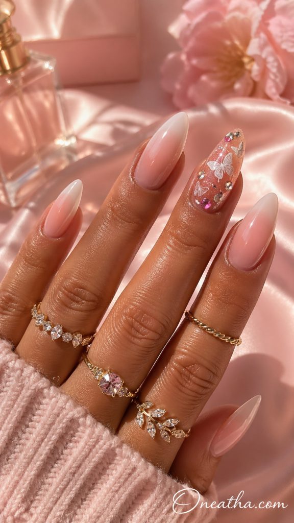 Butterfly nail designs by Oneatha featuring soft pink butterfly nail designs with an accent nail, sparkly base, and rhinestone details, cute butterfly nail designs you need for every season with a feminine and elegant finish.