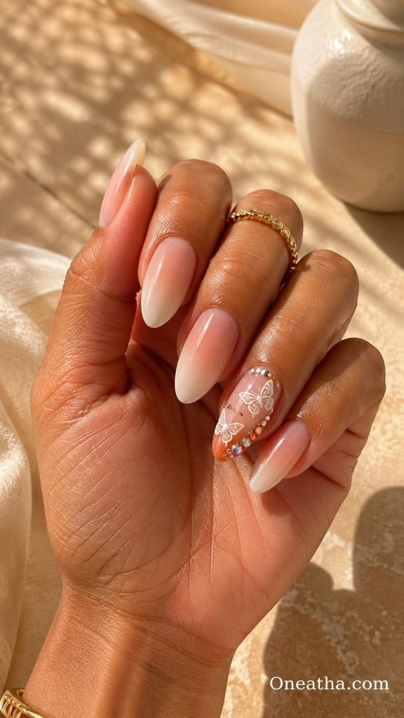 Butterfly nail designs by Oneatha featuring summer butterfly nails with orange creamsicle-inspired tones, ombré glow finish, and an accent nail decorated with orange rhinestones for a bright seasonal nail design.