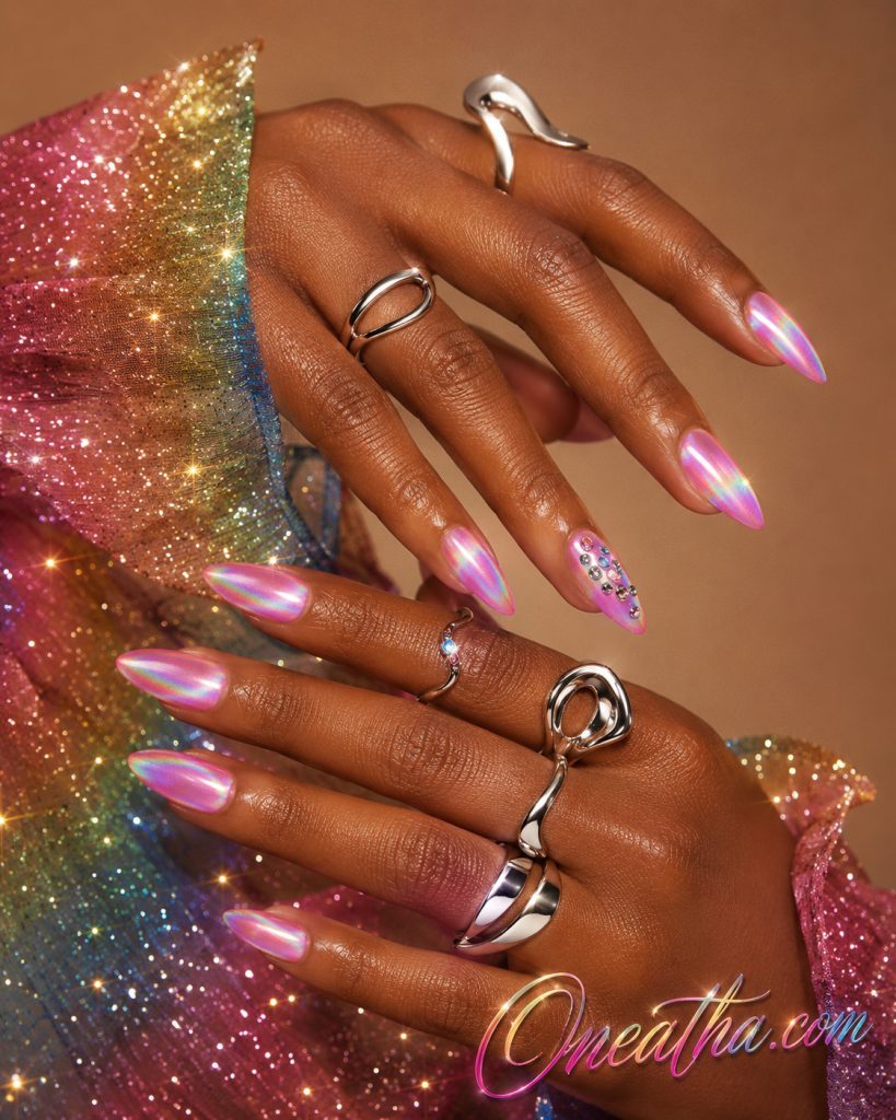 Pink cat eye nails by Oneatha featuring a rainbow holographic shimmer on almond-shaped nails with a glossy gemstone accent nail, silver luxe rings, and a sparkling rainbow blouse against a tan luxury background.
