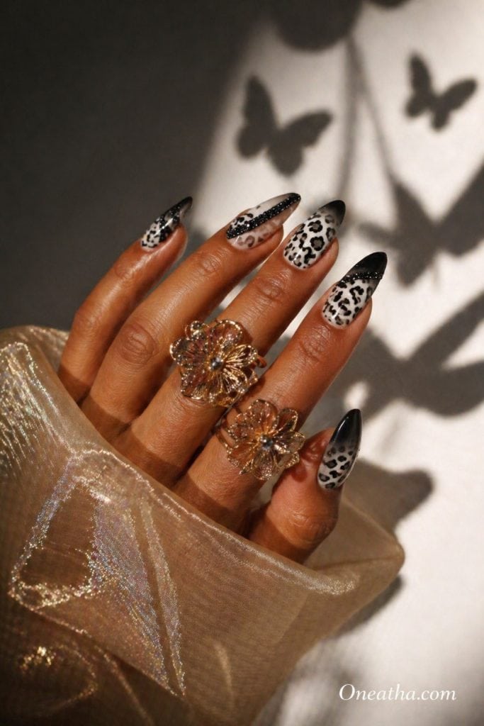 Leopard nails by Oneatha featuring black rhinestone accents, glossy luxury acrylic finish, and bold high-end nail art design.