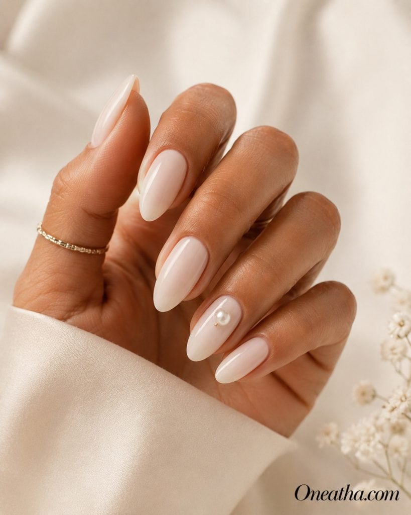 Luxury nail designs by Oneatha featuring glossy almond-shaped nude nails with an elegant pearl accent. This sophisticated manicure is perfect for brunch, tea parties, bridal showers, and timeless everyday luxury.