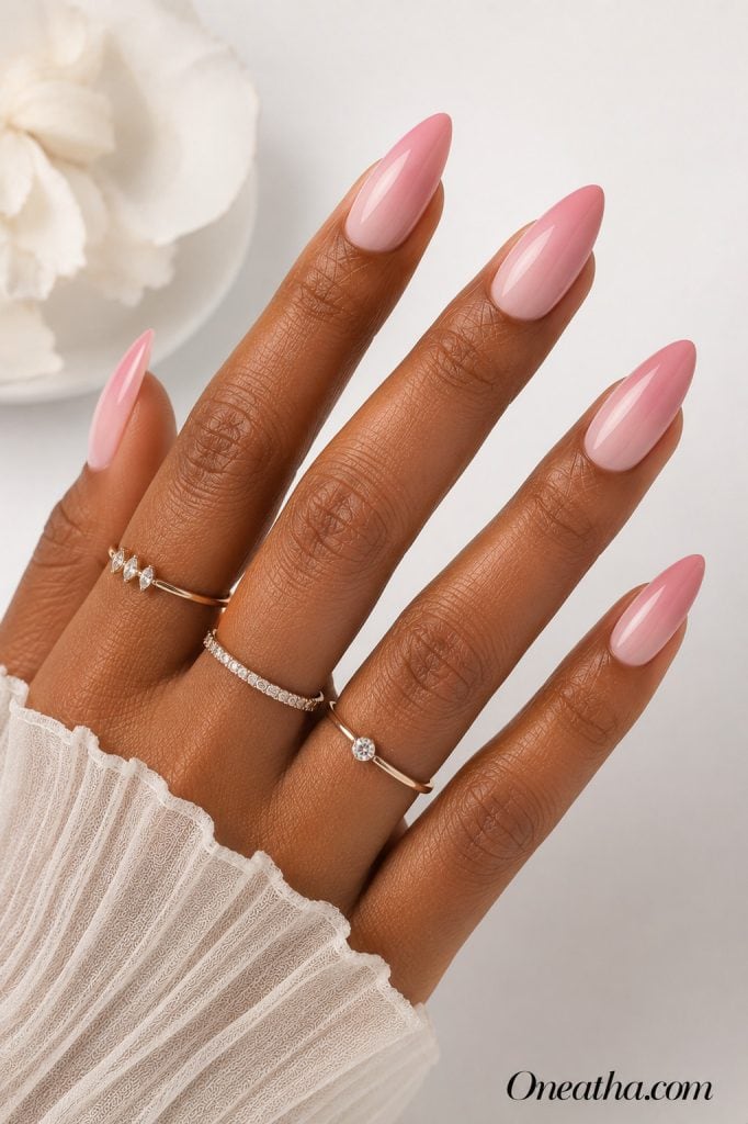 Luxury nail designs by Oneatha featuring glossy blush pink gradient almond nails with a soft ombré fade, delicate rings, and a clean white editorial background.