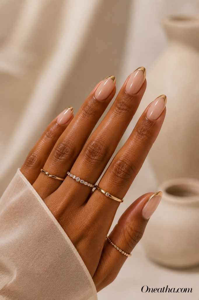 Luxury nail designs by Oneatha featuring sheer nude almond nails with soft gold French tips, glossy finish.