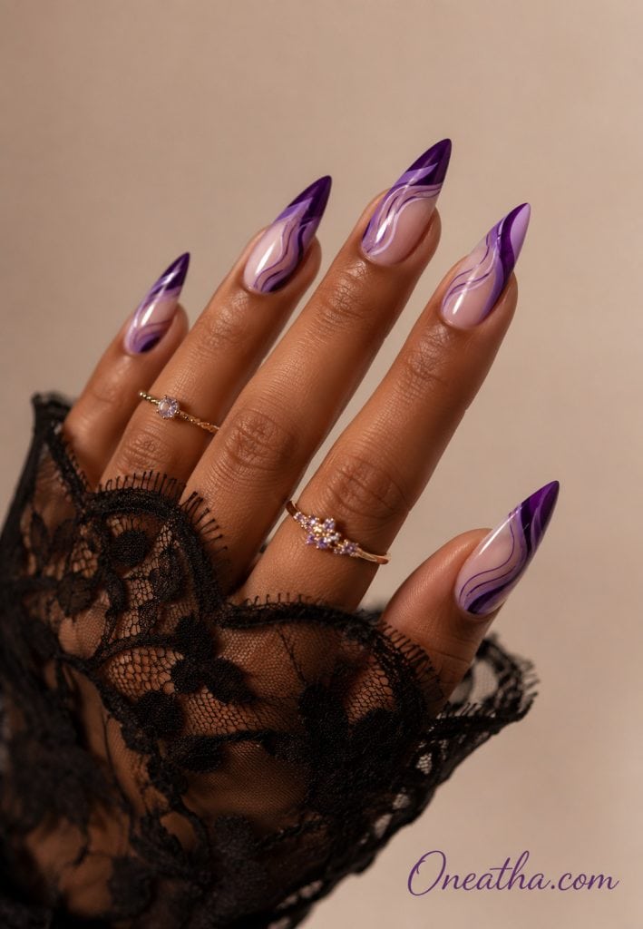 Glossy purple stiletto nails by Oneatha featuring rich violet swirl designs over a soft lilac base, styled with a black lace sleeve on a neutral background.