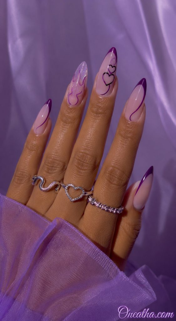 Glossy stiletto nails by Oneatha featuring soft lilac nude polish, deep purple accents, delicate purple and black heart line art, one glittery accent nail, silver statement rings, and a sheer lavender background.