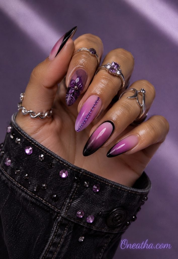 Glossy almond nails with black and plum shimmer, lilac details, and purple gemstone accents by Oneatha.