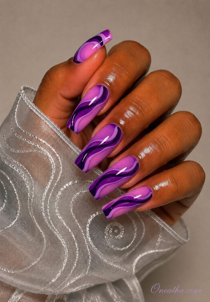 Glossy purple swirl coffin nails by Oneatha with layered lilac and deep violet abstract nail art.
