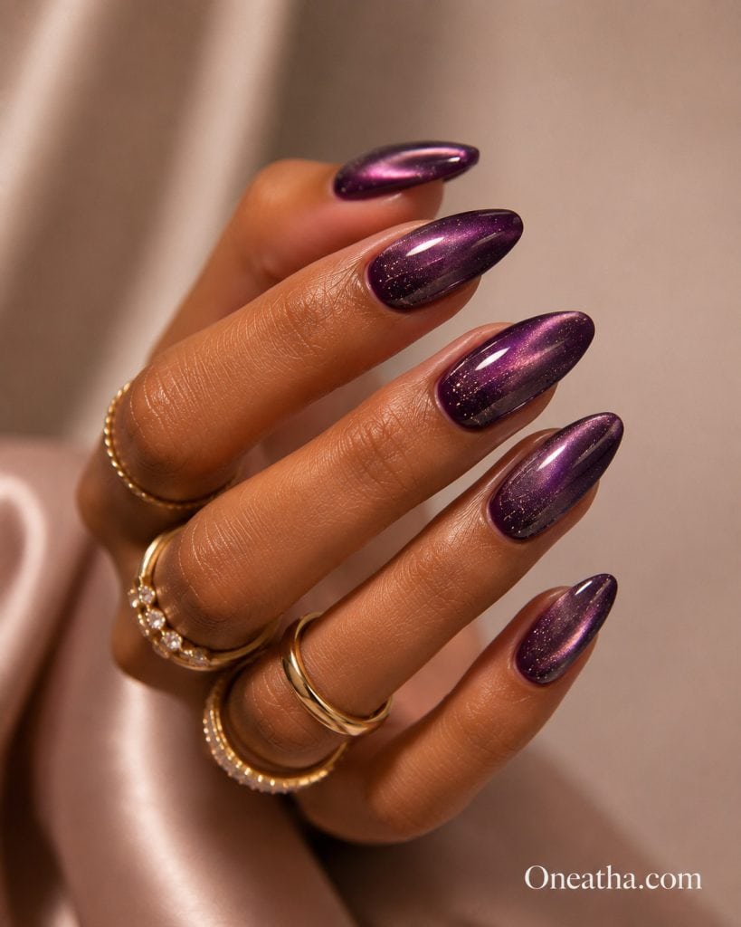 Glossy plum and soft pink cat-eye almond nails with a radiant violet shimmer, styled with gold rings by Oneatha.